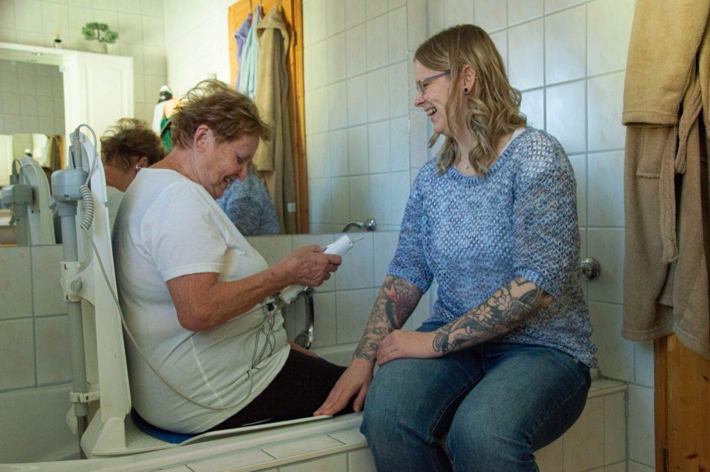 Pflege und Betreuung zu Hause. Pflegerin zeigt Patientin in der Badewanne den Wannenlifter